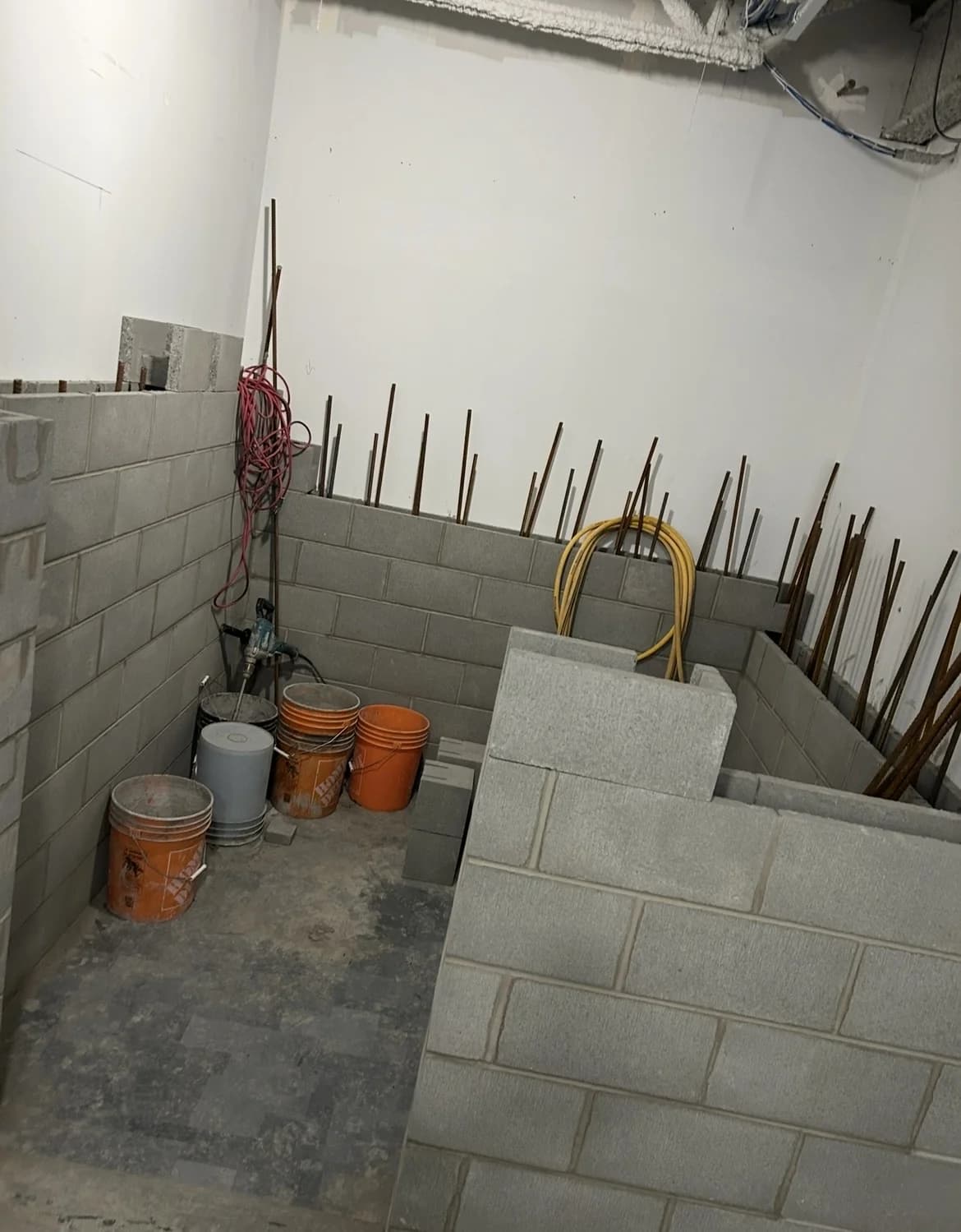 Concrete-block core walls mid-build with rebar dowels, grout buckets and a mixing drill