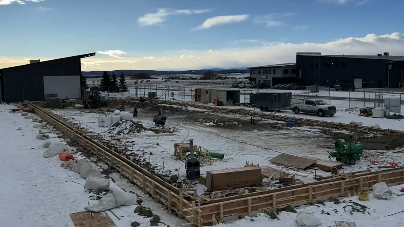Foundation formwork perimeter on a snowy site with construction heaters and lumber staged