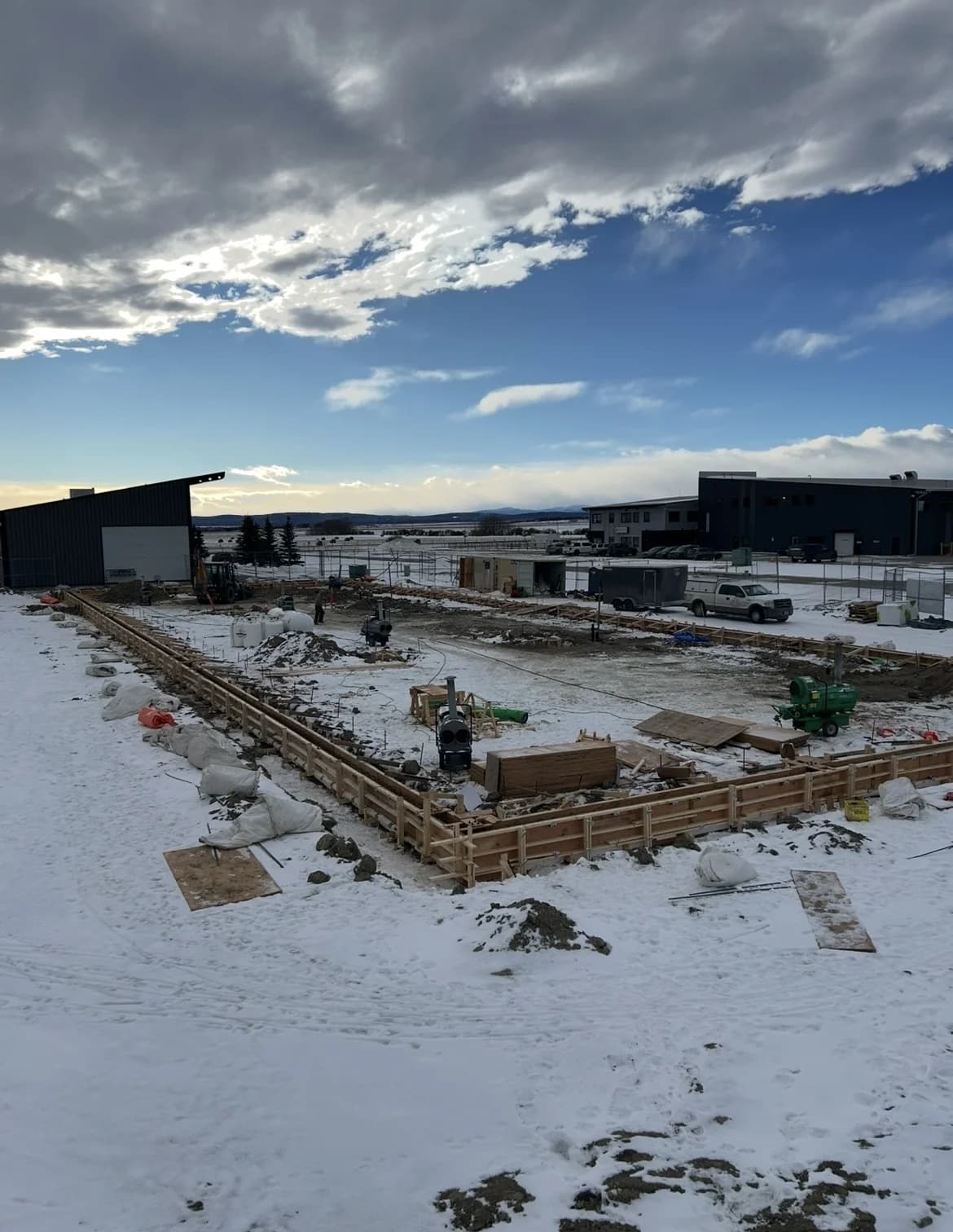 Foundation formwork perimeter on a snowy site with construction heaters and lumber staged