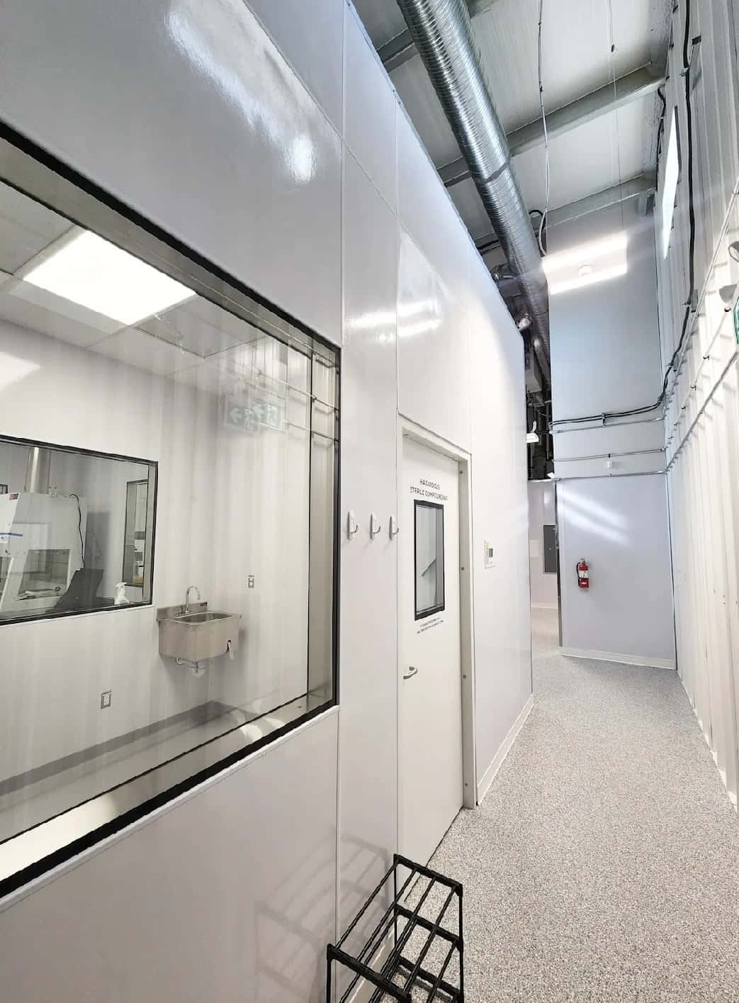 Cleanroom corridor with glossy panel walls, stainless handwash sink and a sterile compounding door
