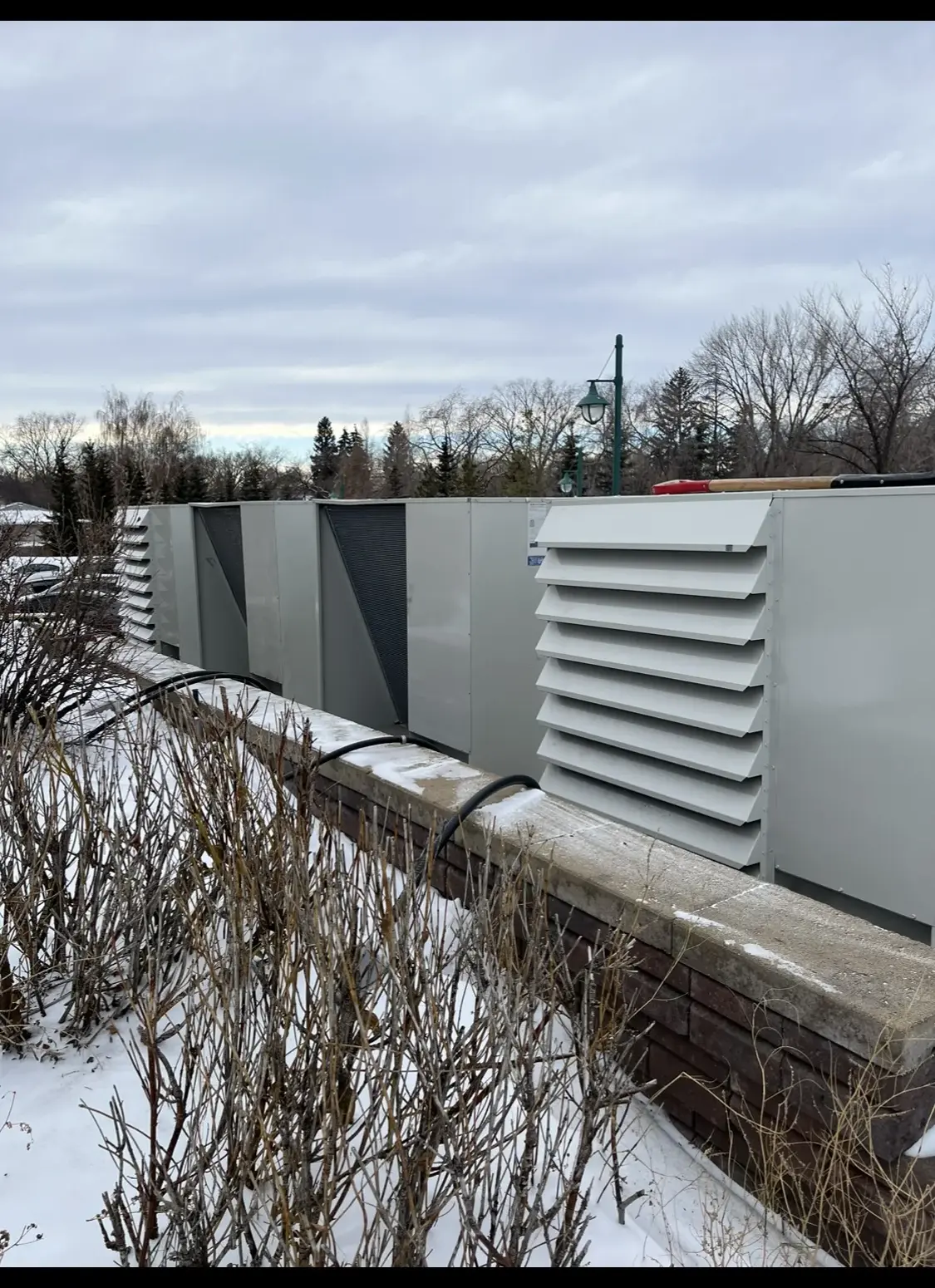Bank of condensing units lined up behind a masonry screen wall in winter