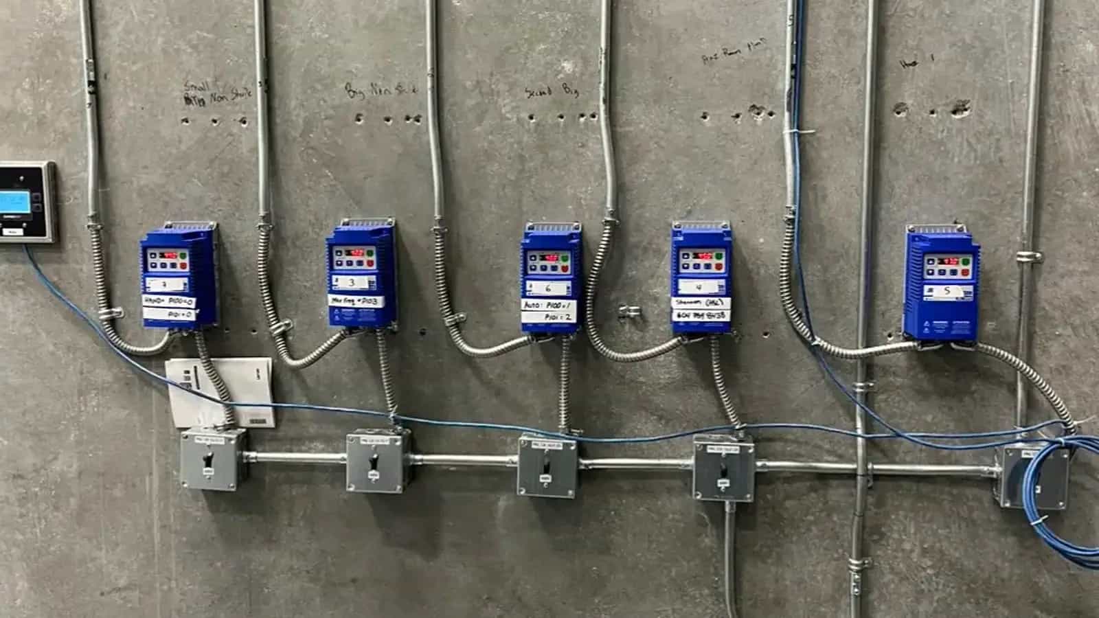 Row of labelled variable-frequency drives with conduit runs on a concrete wall