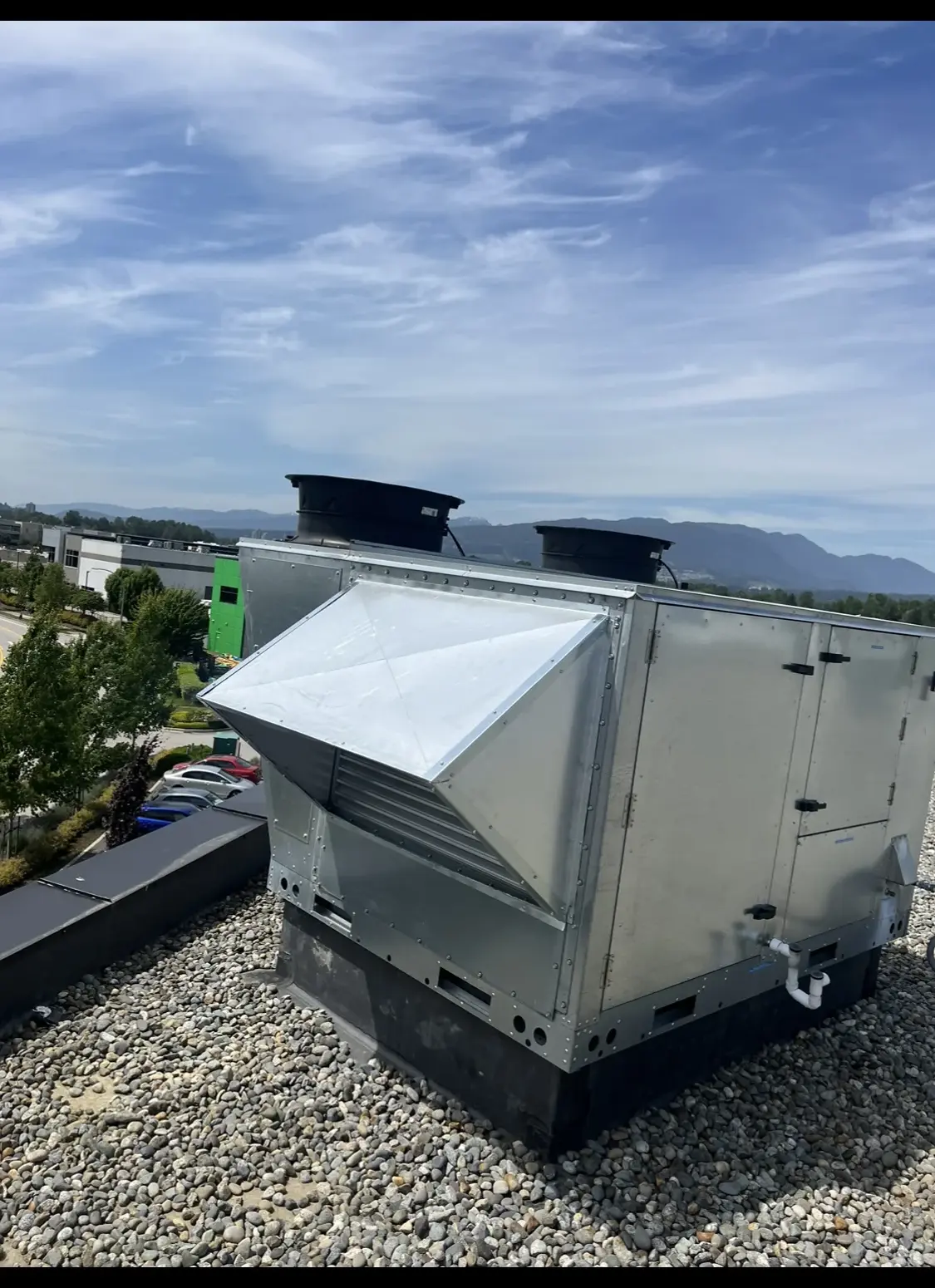 Rooftop air unit with weather hood and exhaust fans on a gravel ballast roof